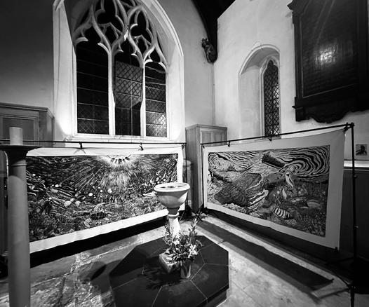Two large modern artworks hang in an ancient church, with arched Gothic windows behind and a font in the foreground. The artworks are black-and-white prints on canvas, both celebrating the beauty and diversity of sealife along with the manmade threats - of plastic and other pollution in the first; various forms of seabed destruction in the second. Atmospheric black and white photo, taken by the vicar after a harrowing day and a midnight hang: peace reigns.