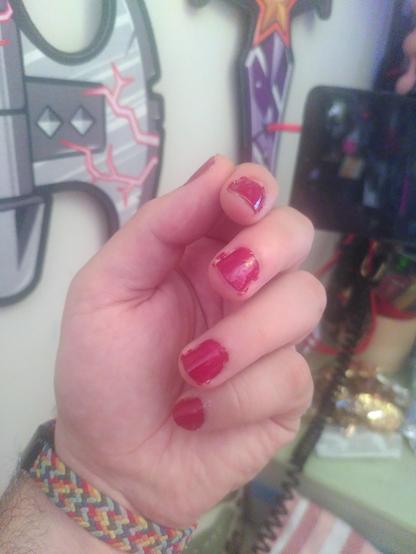 Photo of my hand with "brick" red nail paint. It's a very deep red, slightly on the dark side. In the background are two foam lego weapon, a ninjago axe with red thunder effect and a dreamzzz crystal sword