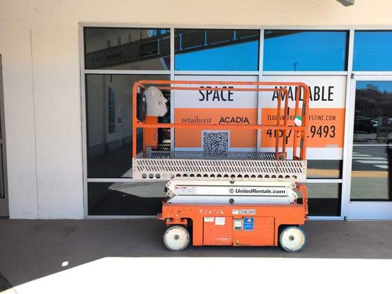 Parked scissor lift vehicle at a mall with a "space available" sign behind it. The controls for the lift mechanism have a metal panel like a face silhouette