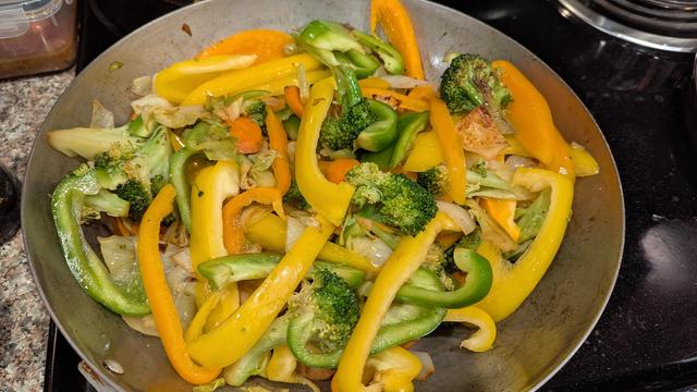 Picture of a 17 inch work filled with broccoli, onion, cabbage, carrot, and 3 colors of bell pepper (green, yellow, orange). Some of the veggies look seared for the stir fry