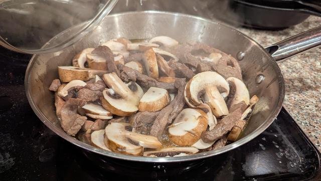 Picture of stir fry beef and thick sliced baby Bella mushrooms in a skillet on a stove