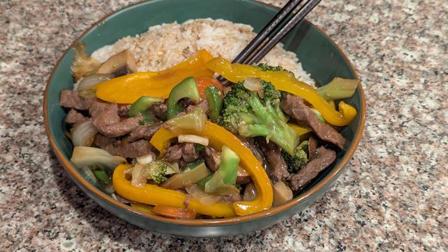 A shallow, but wide, green ceramic bowl with a light brown rim. The stir fry is in the front of the bowl backed by a small mound of white rice with some of the brown sauce drizzled on it. Some chopsticks are sticking out of the bowl stylishly because sometimes I like to be basic