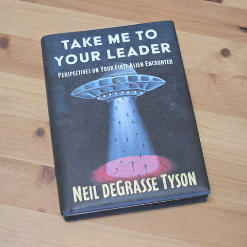 Book on a table titled "Take me to your leader: perspectives on your first alien encounter" by Neil Degrasse Tyson
