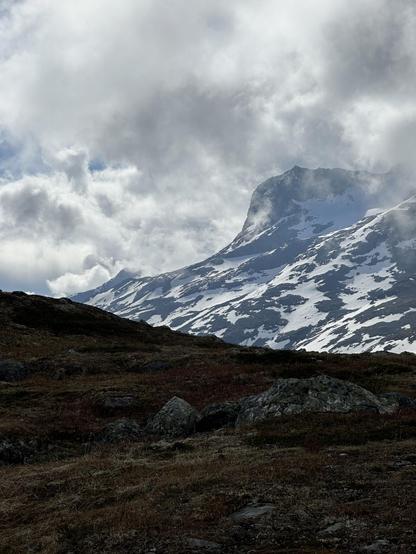 A snow-flecked mountain behind a darker rocky foreground with moody grey clouds above.