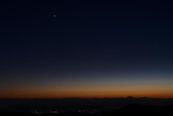 It's late evening twilight, but there is still a band of orange and yellow in the sky along the distant mountainous horizon. The rest of the sky is a dark blue.

The lights of the village of La Luz are visible on the floor of the Tularosa basin.