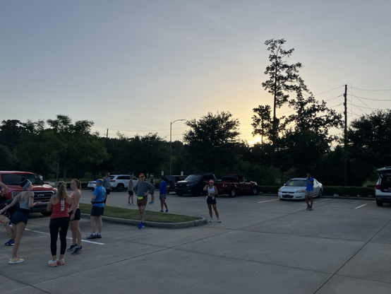 Sunrise and some dark trees; runners stretching and warming up in a parking lot