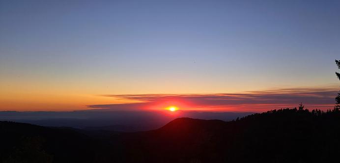 A wide field view of the sunset and forest fire smoke plume. Blue sky is above the smoke plume. Foreground is a dark silhouette.
