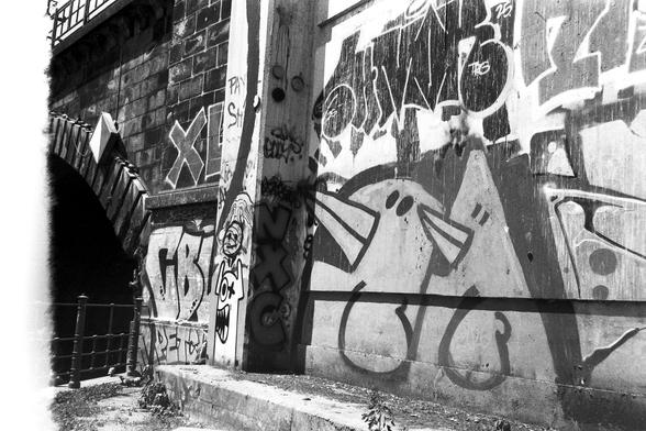 A railway bridge in Berlin.  There are graffiti on this bridge of two very stylised birds.  They are very adjacent in style to the graffiti birds to be found on the Hitman 3 Berlin level, which is what drew my eye to them.  The light that day was VERY harsh and it was 36C at the time.  The camera is appears light leaks and the left hand side of the image has a bright white band where light has attacked the film emulsion.  I have left it alone because it suits the aesthetic.