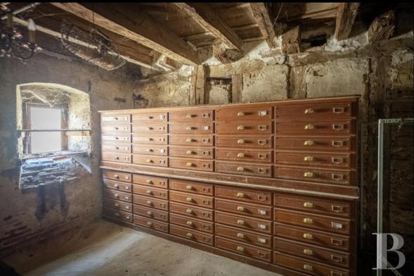 Beautiful piece of dark-honey-coloured furniture, made up of five rows of narrow drawers, each 10 deep, with brass handles and brass card holders. It’s in a room with wooden beams and a small window.