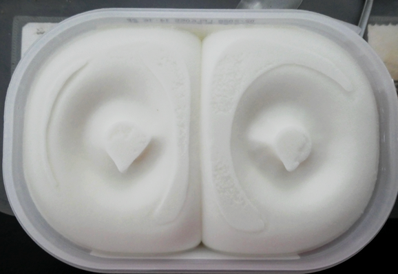 une boite rectangulaire aux cins arrondis de glace au citron vert, ouverte, le dessus de la glace fait comme deux moitiés de visage avec au milieu comme deux yeux, on dirait une chouette toute blanche.