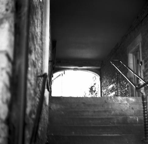 A very old set of steps leading up to an old arched over street.  In the middle of the set of steps is a recently added (well in the last 100 years)  metal hand rail.