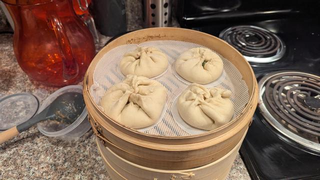 Picture of a kitchen counter with bamboo steamer baskets stacked. Some un cooked buns are sitting in the top steamer basket