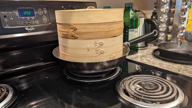 Picture of an electric stove with a wok on the back burner. The streamer baskets are stacked and sitting in the wok