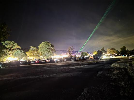A far view of the festival ground at night time with a green laser shining far into the sky
