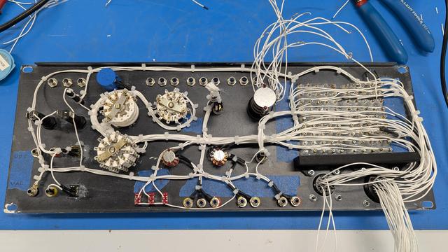 Picture of the back side of a text fixture panel. There are several today switches placed in y'all rows in the middle of the panel. On the top you can see a row of empty LED holders. There are 90 test points on the right with near, clean rows of wires running between the test points. At he bottom right, you can follow wires coming out of the right side of the test points down towards the back side of the two plastic connectors that go to the external harness. Almost all the wiring is cleanly routed and zip tied into a series a bundles.