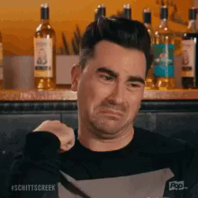 a man is making a sad face in front of bottles of alcohol .