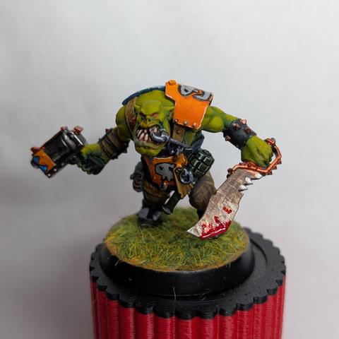 Miniature of a WH40k orc painted with green-yellow skin and orange armor. View from the front.