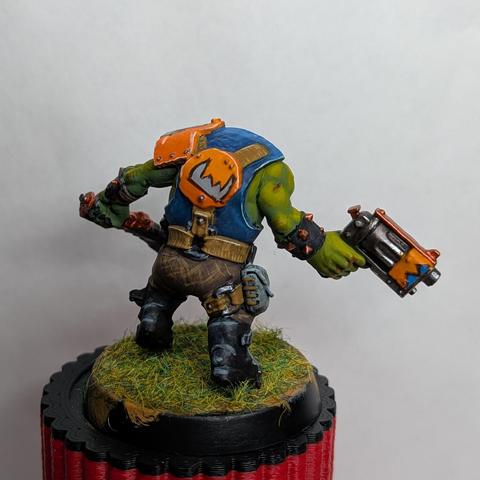 Miniature of a WH40k orc painted with green-yellow skin and orange armor. View from the back.