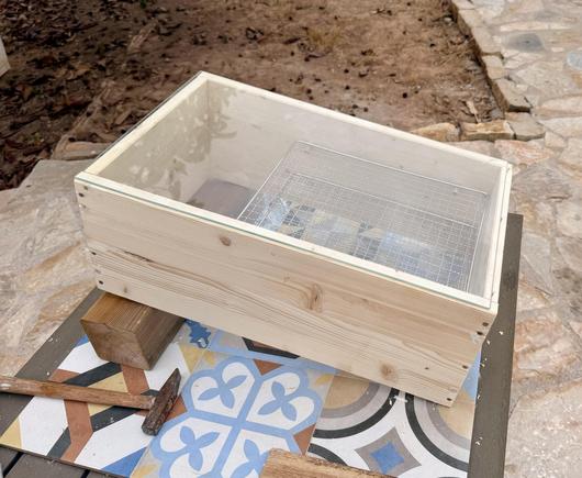 Photo of a woden solar dehydrator with two meshes and a glass tap. Missing the floor mesh and some feet.