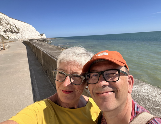 Selfie eines älteren Paars vor sonnigem Meer rechts und gleißend weißen Klippen links.