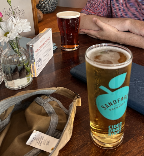 Ein Keipentisch mit zwei gefüllten Pint-Gläsern, auf dem vorderen ist die Aufschrift „Cider“ erkennbar.c