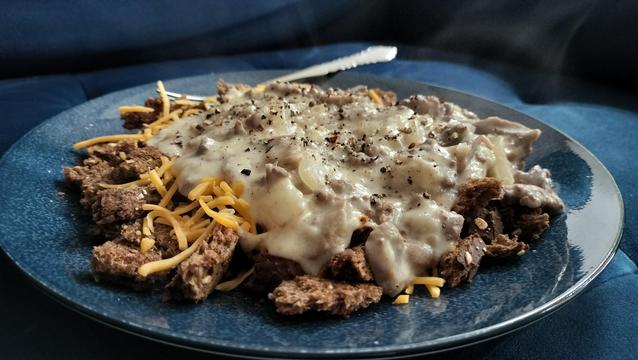 A blue plate containing ground beef, onions, and mushrooms, served over toast with a Mornay sauce.