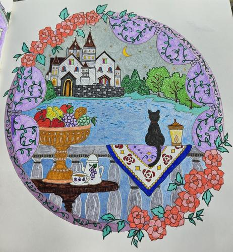Coloring book page of a black cat on a railing looking out onto a lake with a castle in the background. The sky has stars and a crescent moon. There is a tall fruit bowl near the cat. The image is framed in a circle with flowers and vines circling around it.