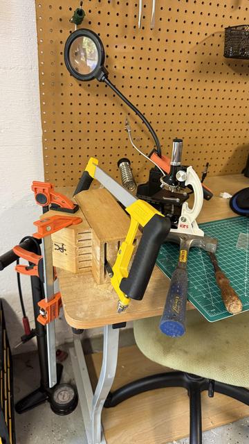 A knife block held to a desk with a clamp with a hack saw blade in one of the knife slots. A hammer and chisel is nearby along with various other items that were shifted around due to sawing.