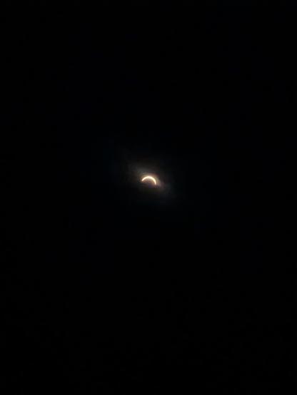 Amateur photo of the solar eclipse. A very thin yellow arc is visible on top of a very dark background.