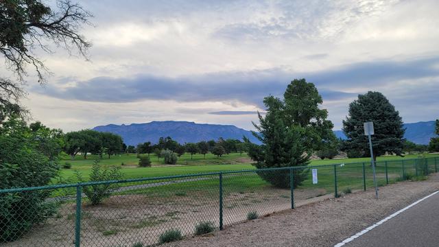 Cold blue mountains under a steel sky of gleaming clouds. The green of the golf course looks saturated under diffuse light like this, a hyper-vivid color.