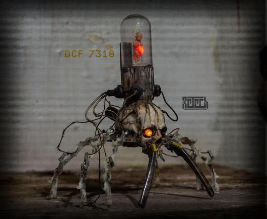 A skull with mech legs and a foetus in a clear chamber on top. Various wires and other bits are connected.