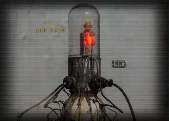 A skull with mech legs and a foetus in a clear chamber on top. Various wires and other bits are connected.