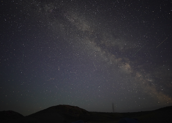Perfectly dark hills silhouetted by the Milky Way diagonally across the perfectly dark sky.  There are easily a dozen satellite streaks visible.