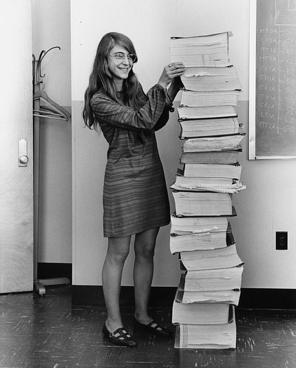 black and white photo of a woman standing next to a stack of paper taller than she is.
