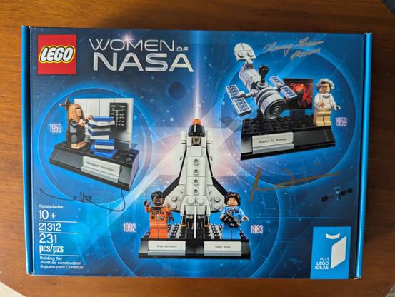 A Women Of NASA LEGO kit with a representation of the iconic photo of Margaret Hamilton next to a stack of printout binders signed by (among others) Margaret Hamilton herself.