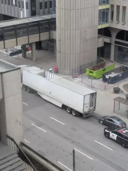 An 18-wheel truck with its rear door bashed open and significant damage to the roof.