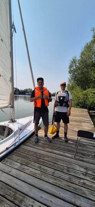 Two guys standing on a dock in front of a dinghy.